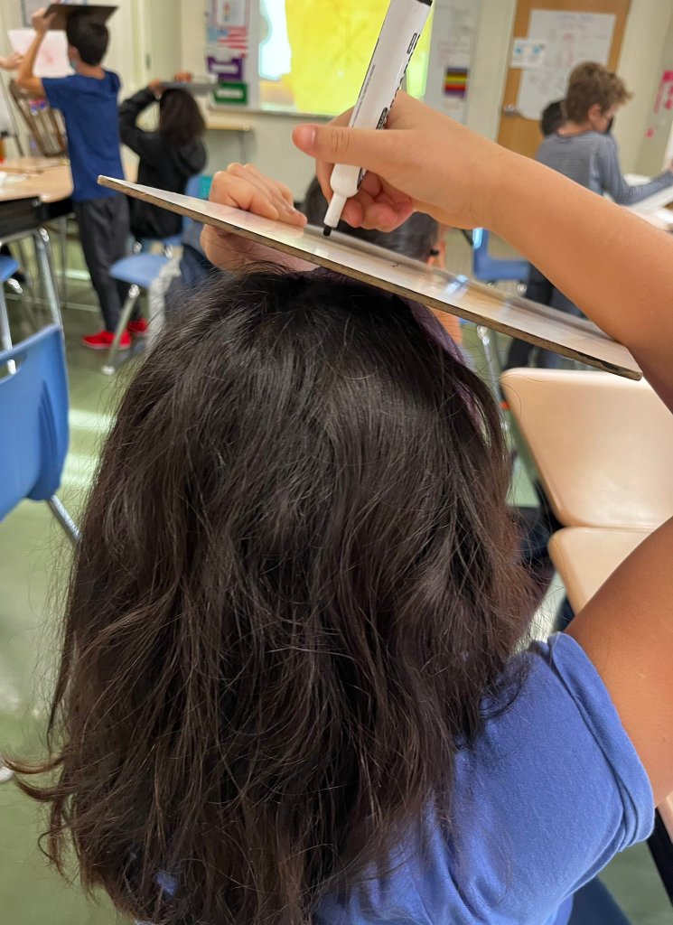 Students balance whiteboards on their heads, and draw snowmen.