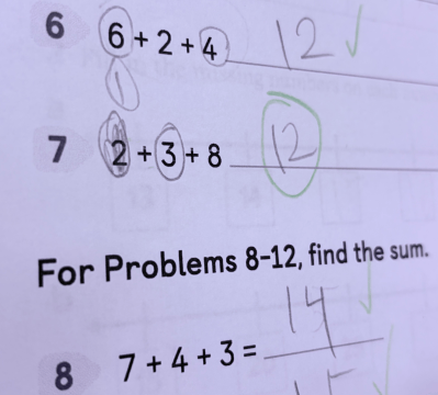 A worksheet showing addition problems. 6 + 2 + 4 = 12 has a check mark, with the 6 and 4 circled. In 2 + 3 + 8, the 2 and 3 are circled, and the answer 12 is circled in green. 7 + 4 + 3 = 14 has a check mark. Grace strikes again!